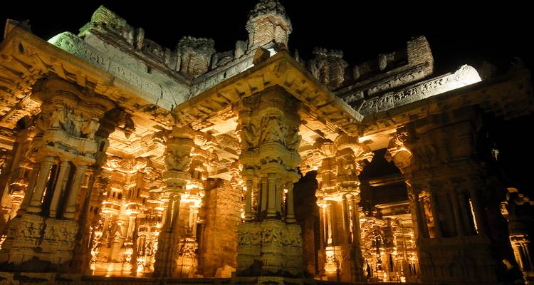 Kunstvoll geschnitzte Tempelsäulen, die nachts beleuchtet sind.