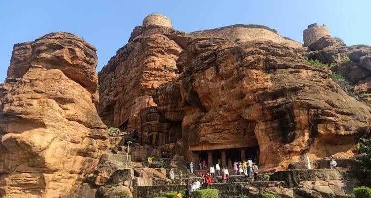 A rocky hill with ancient cave structures and people.