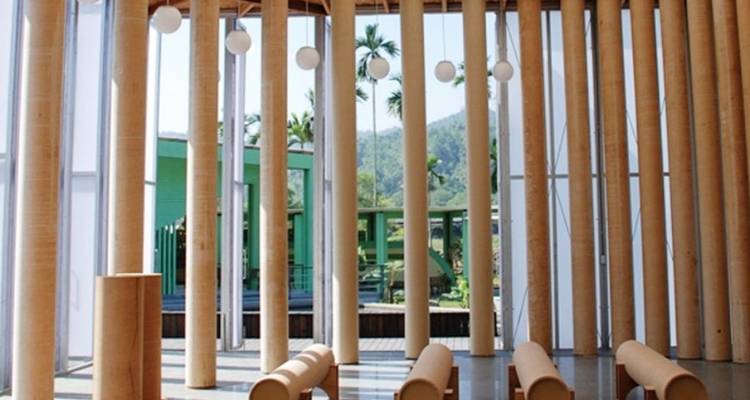Modern interior with tall bamboo columns, hanging lights and benches, looking out toward greenery and hills.
