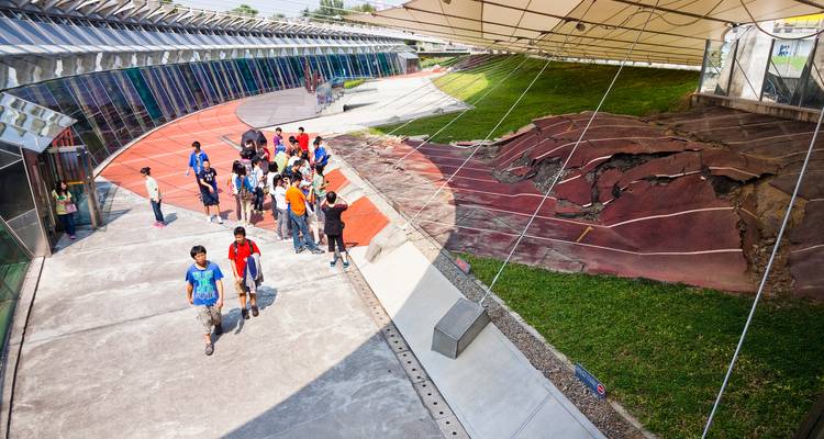 School group walking through a modern glass-roofed earthquake museum showcasing an exposed fault line