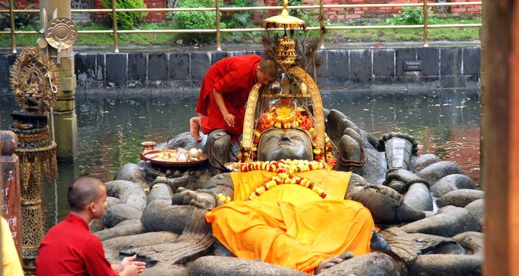 Los monjes realizan rituales junto a una estatua de Visnú reclinada de piedra cubierta con tela naranja en un estanque sagrado.