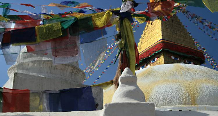 Banderas de oración de colores brillantes enmarcan la base blanca y la aguja dorada de una gran estupa bajo un cielo despejado.