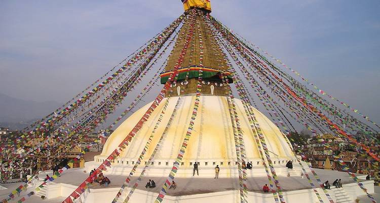 Large white stupa crowned with fluttering prayer flags radiating outward over surrounding rooftops.