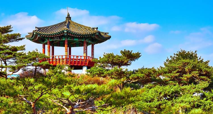 Colorful traditional Korean pavilion over a landscape with blue sky.