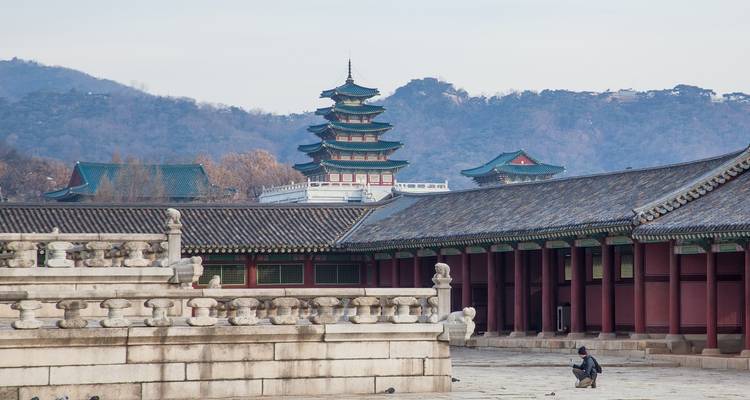 People sitting in front of traditional Korean architecture with mountains in the background.