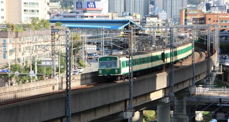 Train moving on elevated tracks in an urban area with buildings around.
