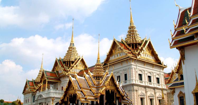 Verzierte Dächer und vergoldete Spitzen des Großen Palastes von Bangkok vor einem blauen Himmel.