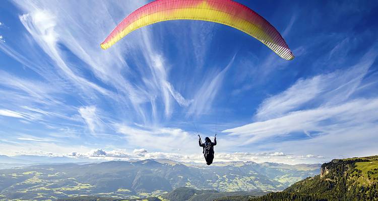 Paraglider above mountainous landscape with a sunny sky.