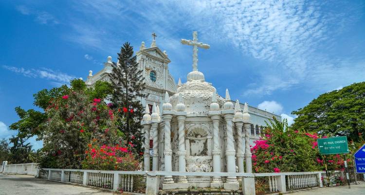 White-walled church surrounded by vibrant flowers under a blue sky.