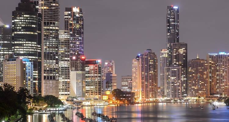 A nighttime cityscape with illuminated skyscrapers reflected in the river.