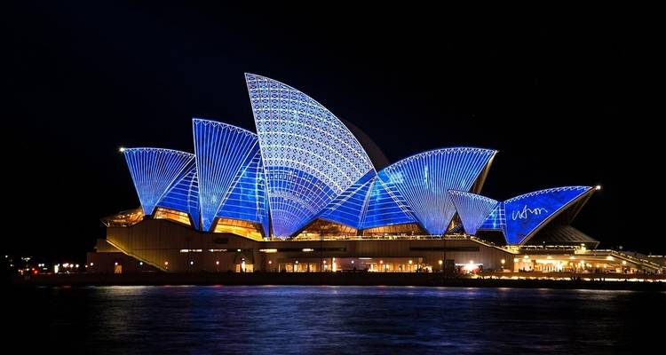 The Sydney Opera House illuminated at night with reflections on the water.