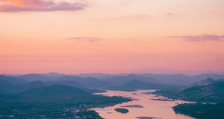 Serene pastel sunset over a winding river and distant misty hills.