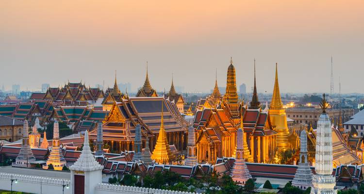 Illuminated spires of Bangkok’s Grand Palace complex glow at twilight.