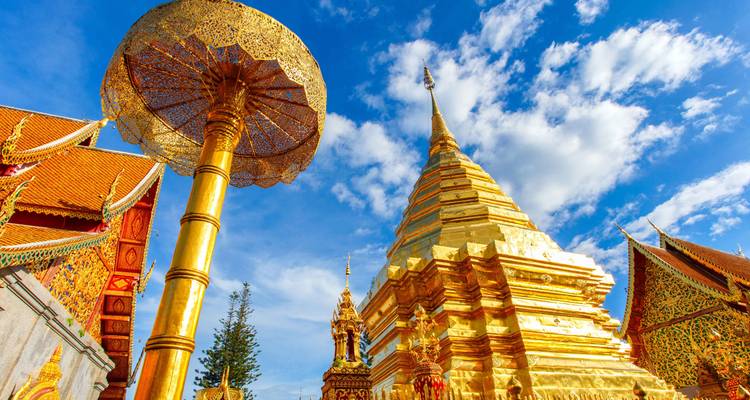 Upward view of gilded stupa and ceremonial umbrella against a vivid blue sky.