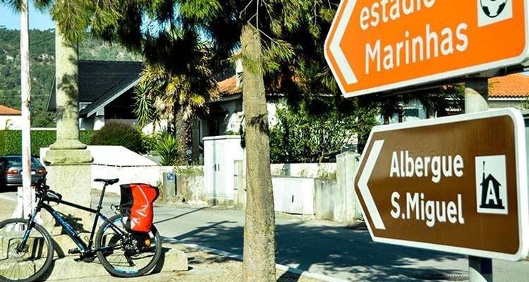 Een toerfiets leunt tegen een stenen paal bij kleurrijke camino-wegwijzers op een zonnig straatje.