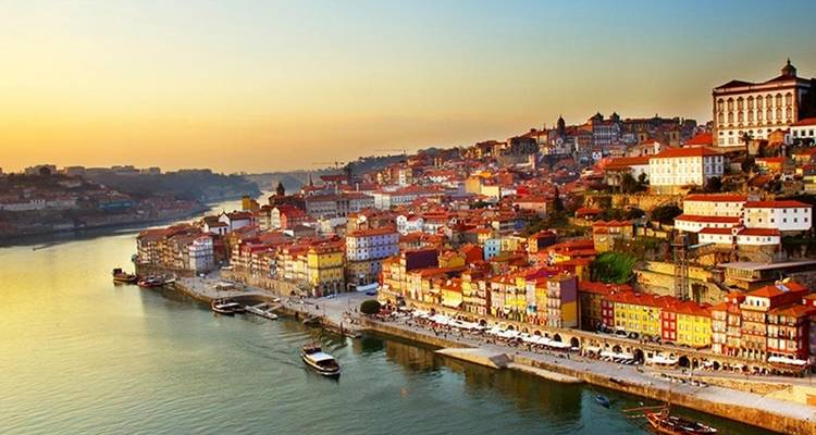 Panoramisch uitzicht bij zonsopgang over Porto's kleurrijke riviergebouwen langs de Douro-rivier.