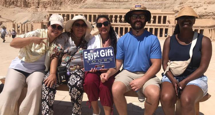 Friends seated on bench holding tour sign with Hatshepsut Temple terraces behind.