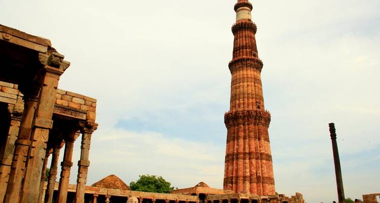 Qutub Minar, ein hoher Backsteinturm in Delhi, umgeben von Ruinen.