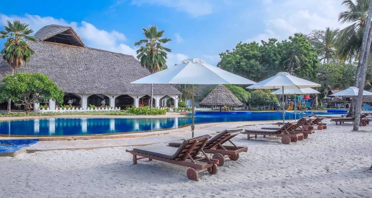 Poolside with loungers on a sandy beach at a resort in Zanzibar.