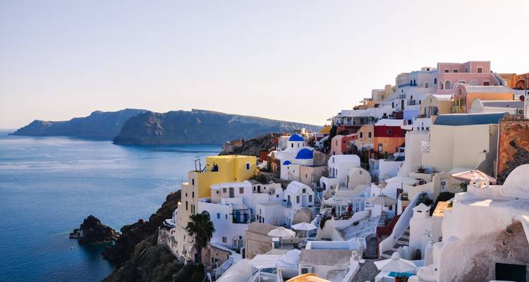 Classic Santorini caldera view with pastel houses cascading down cliff toward blue Aegean Sea