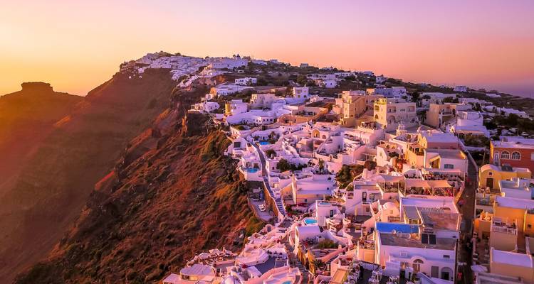 Aerial sunset glow over Santorini's cliff-side villages with dramatic caldera backdrop