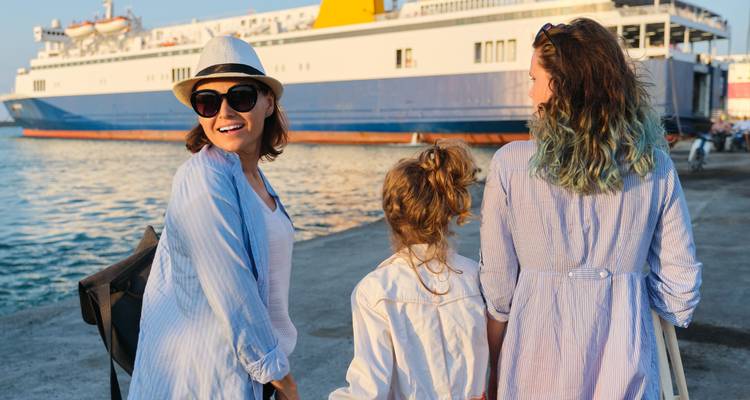 Smiling woman with hat and sunglasses with two girls near ferry docked at harbor