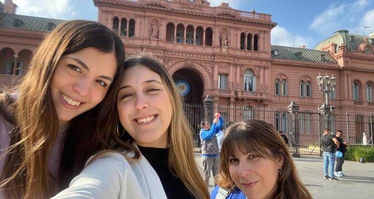 Three women smiling in front of a historic building.