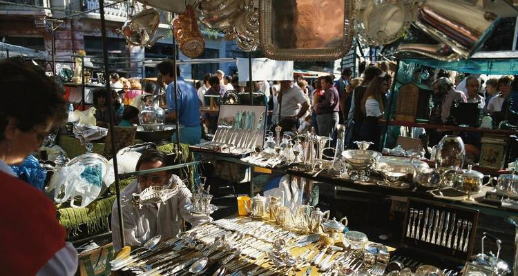 Mercado concurrido con platería en exhibición y gente navegando.