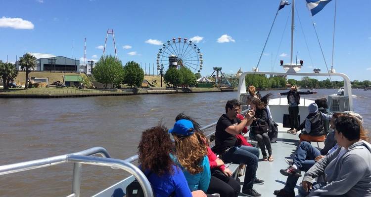 Grupo de personas disfrutando de un paseo en bote por un río con un parque de diversiones a la vista.