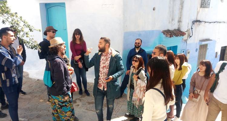 Guide touristique s'adressant à un petit groupe de touristes dans une ruelle étroite aux murs peints en bleu