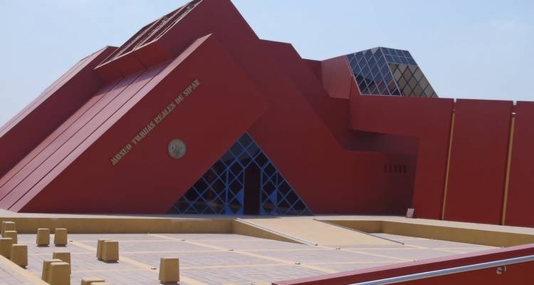 Modern rood geometrisch museumgebouw in een parkachtige omgeving.