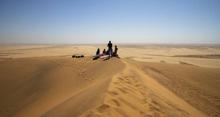 Gruppe von Personen auf Sanddünen mit Surfbrettern.