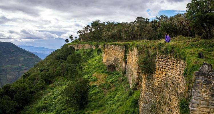 Person, die am Rand einer üppig grünen Klippe geht.