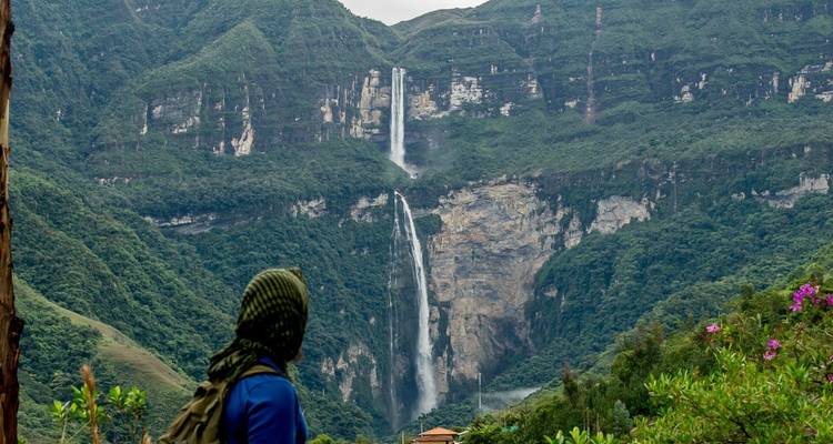 Person, die einen hohen Wasserfall in einer üppig grünen Landschaft betrachtet.