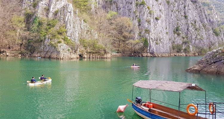 Vue panoramique de kayakistes sur un lac avec des montagnes rocheuses en arrière-plan.