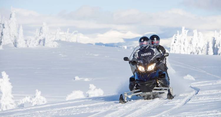 Zwei Personen auf einem Yamaha Schneemobil auf einem verschneiten Feld.
