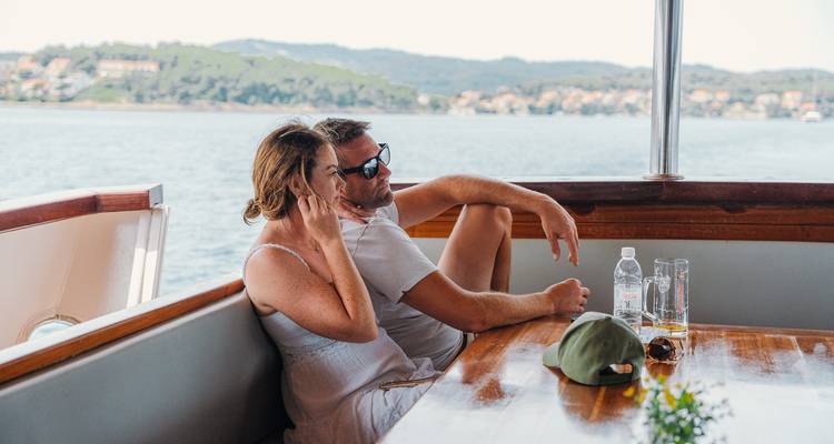 Couple relaxing on a boat with a scenic view of the water and coastline.