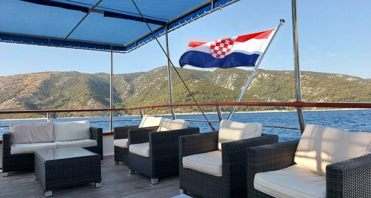 Das Deck eines Bootes mit einer kroatischen Flagge und einer Bergkulisse im Hintergrund.