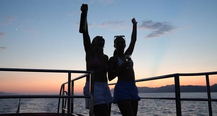 Silhouettierte Figuren auf einem Boot bei Sonnenuntergang, die mit ausgestreckten Armen feiern.