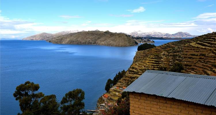 Der tiefblaue Lago Titicaca, umgeben von terrassierten Hängen und entfernten schneebedeckten Gipfeln