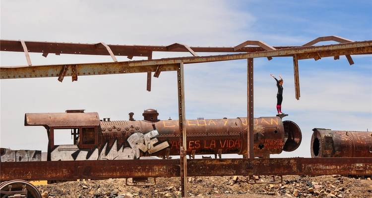Rostende Lokomotiven auf dem Zugfriedhof von Uyuni mit einem Reisenden, der auf einem Balken balanciert