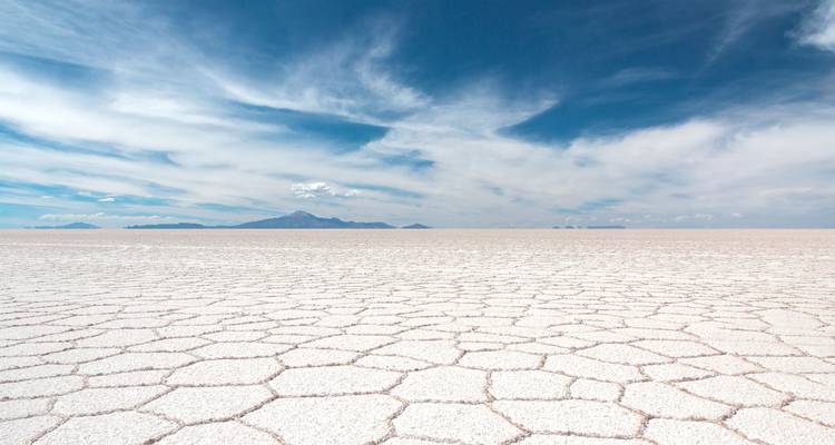 Formaciones de sal hexagonales en el Salar de Uyuni con montañas en la distancia.