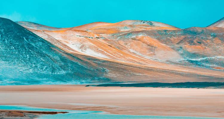 Montañas desérticas coloridas con nieve en las cimas y cielo despejado.