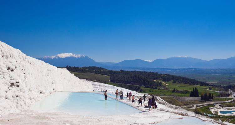 Menschen, die auf weißen Travertinterrassen voller Wasser gehen.