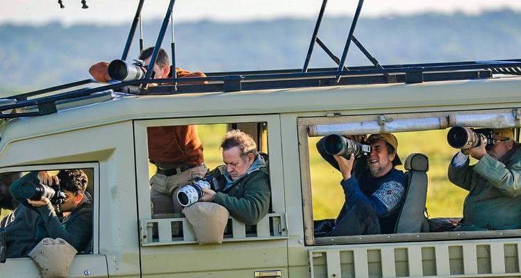 Photographers with telephoto lenses aim from open-roof safari vehicle during game drive