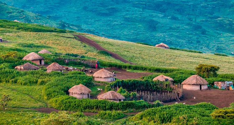 Scattered thatched huts of a Maasai village nestle in lush green hillside at dawn