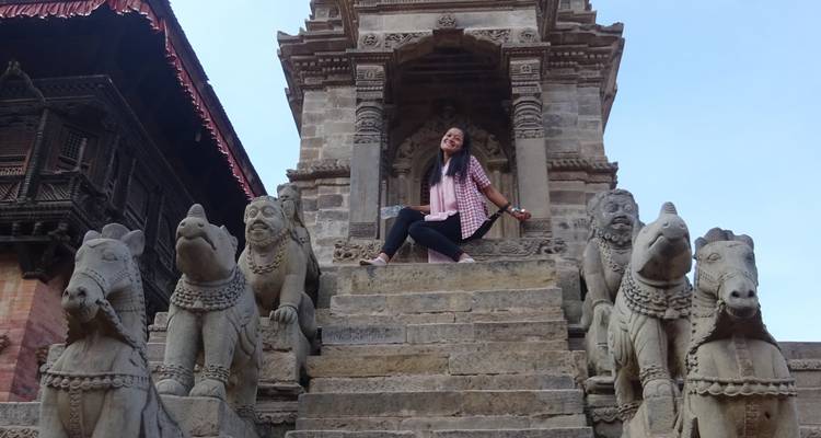 Person, die auf den Stufen eines alten Tempels sitzt, mit Tierskulpturen entlang der Treppe.