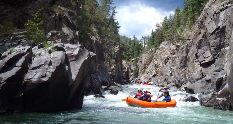 Orange rafts navigate churning whitewater through a narrow rocky gorge lined with pine trees near Durango