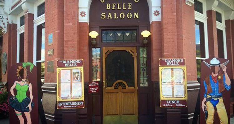 Historic brick-fronted Diamond Belle Saloon with decorative cut-out cowboys and show posters flanking the entrance