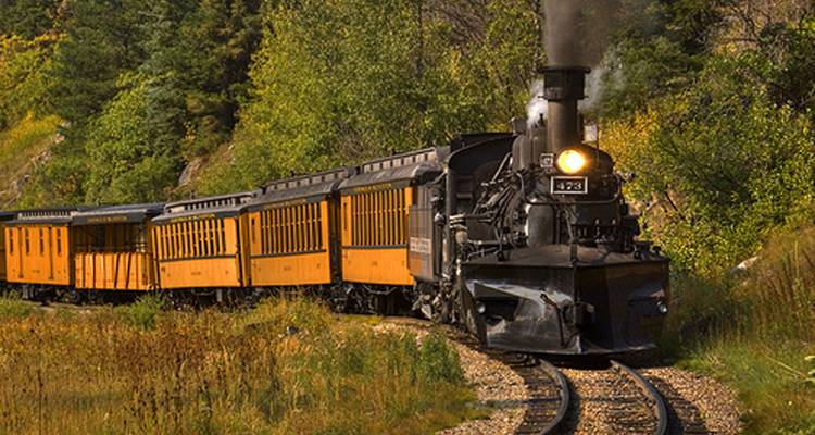 Vintage steam locomotive with yellow carriages rounded by pine forest on the Durango & Silverton narrow-gauge track